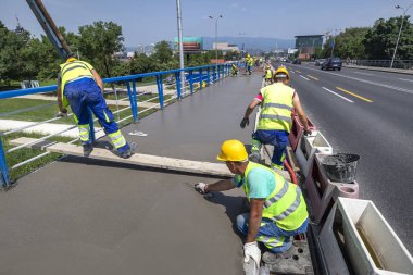 Taze pürüzsüz gri beton. Trafik saatlerinde köprüde kaldırım kaplamasını tamamlayan bir grup inşaat işçisi