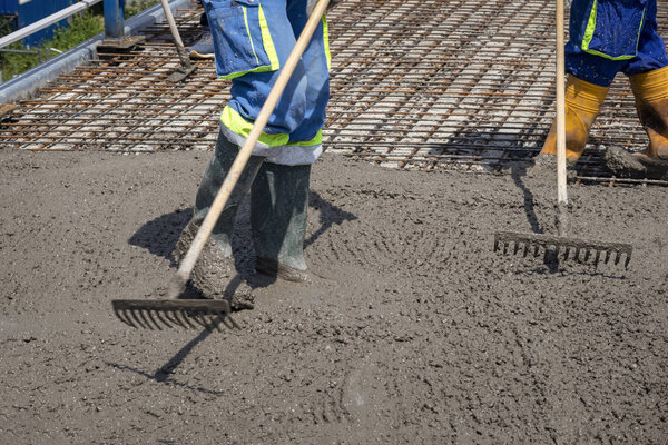Construction worker spreading freshly poured concrete mix on the bridge with rake, repair sidewalk on bridge in Zagreb, Croatia