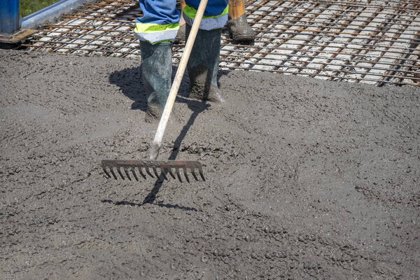 Construction worker spreading freshly poured concrete mix on the bridge with rake, repair sidewalk on bridge in Zagreb, Croatia