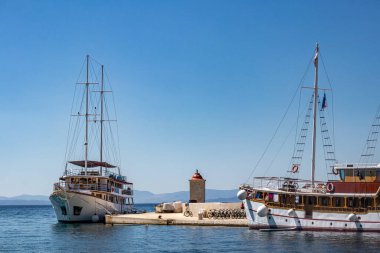 Hırvatistan 'ın Brac adasındaki Postira köyünün liman ve iskelesinde turist, balıkçı tekneleri ve deniz feneri bulunuyor. Dalgakıranda kayıklar ve deniz feneri.