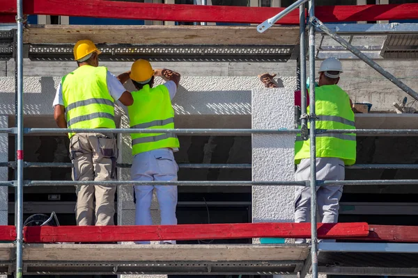 İşçiler taş kaldırım taşıyla yeni beton cephe oluşturuyorlar. Kırmızı, beyaz ve mavi çizgiler.