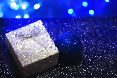 Gümüş hediye kutusu ile bir yay ve kalpler bir koyu mavi arka plan bulanık. Güzel parlak hediye kış tatilleri için.