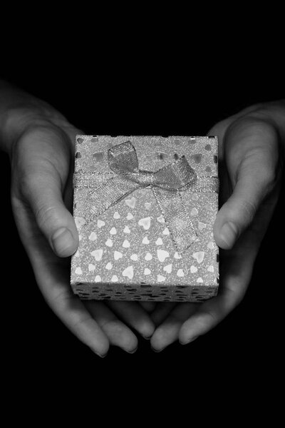 Черно-белый цвет подарочная коробка с луком и маленькие сердца в руках женщин на темном фоне. Искренний подарок на все праздники. Концепция заботы о матери, семейный подарок
.