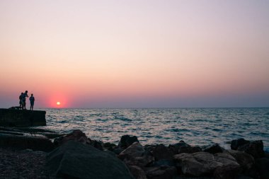 Ufukta balıkçı erkeklerle deniz plajında gün batımı.