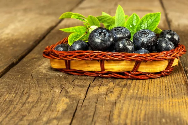 Wet blueberries in a small wicker basket. Freshly picked forest fruits on a wooden table. Sales of blueberries. Healthy summer refreshment