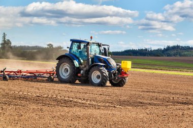 Mavi bir traktör tahıl ekiyor. Çek Cumhuriyeti'nde bir çiftlikte çiftlik işi. Buğday tarlasında traktör. Tarım makineleri.