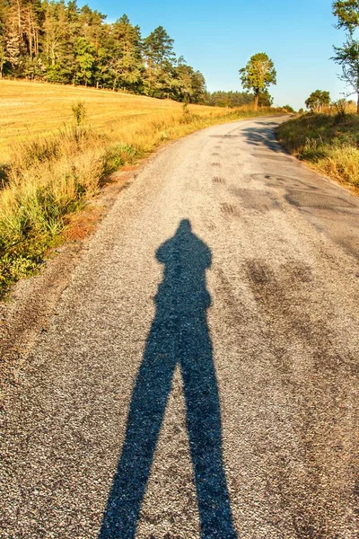Чоловіча тінь на дорозі. Ранкове сонце на асфальтовій дорозі. Літній ранок. Заміська дорога вранці . — стокове фото