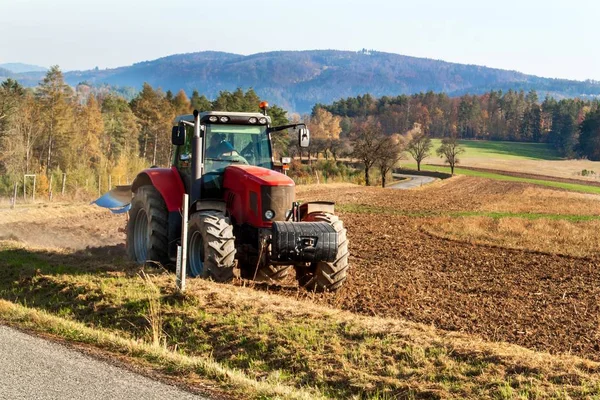 Rode tractor ploegt veld. Landbouwwerkzaamheden op een boerderij in Tsjechië. Herfstlandschap. — Stockfoto