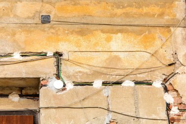 Duvardaki alçının altında elektrik kabloları var. Tuğla duvardan sarkan elektrik kabloları. Bir aile evinin yeniden inşası. Elektrik kablolarının tamiri.