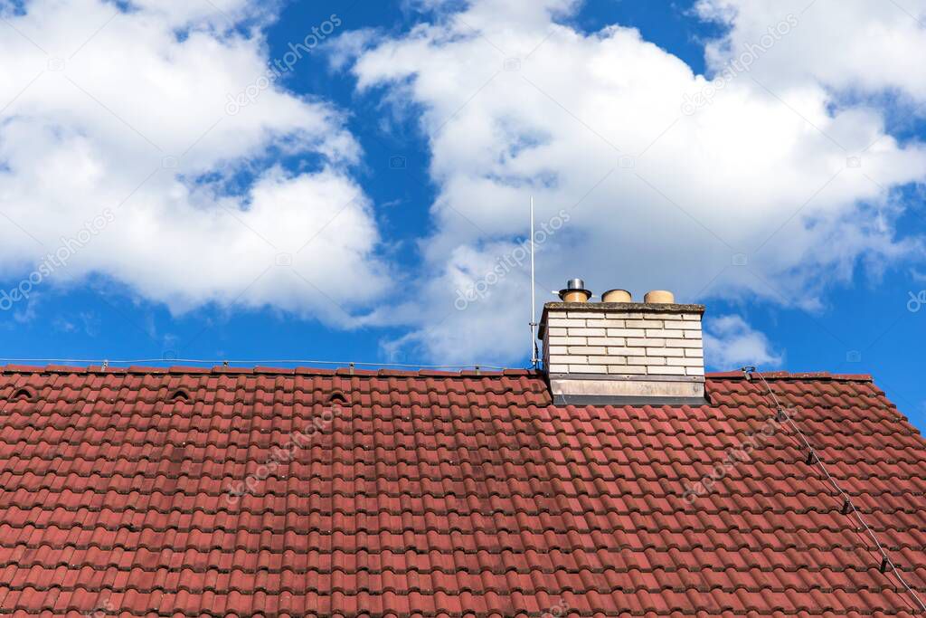 Brick chimney on the roof of a house against the blue sky. Environmental protection concept. Air pollution.