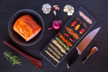 Siyah ahşap arka planda çiğ domuz pirzolası. Baharatlı, biberiyeli, kekik, fesleğen, tuz ve biberli çiğ domuz eti parçaları.