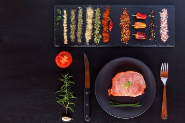 Siyah ahşap arka planda çiğ domuz pirzolası. Baharatlı, biberiyeli, kekik, fesleğen, tuz ve biberli çiğ domuz eti parçaları.