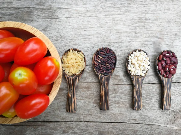 seed on wood spoon and tomato bowl /grains or cereals seeds on wooden spoon various kinds of grains with red kidney bean , Job\'s tears , riceberry and brown rice on wooden background