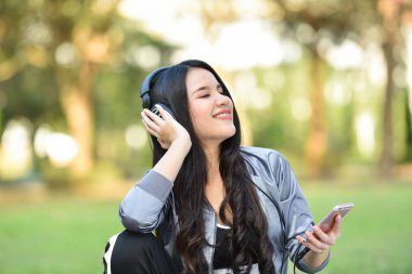 müzik akıllı telefonlar için Dinle / cep telefonu açık mutlu gülümseyen kız ile müzik dinlemek genç kadın egzersiz yeşil bahçe Park kulaklık ile müzik dinlemek rahatla 