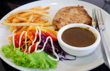 Biftek yemek tabağı / ızgara biftek domuz patates kızartması ve salata sebze domates limon beyaz tabak seçici odak biftek sosu ile