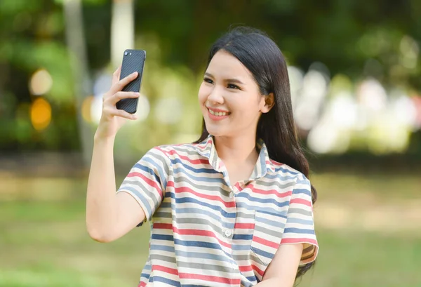 Woman phone happy / Beautiful smiling young girls taking selfie mobile phone camera on park outdoors - happy woman student playing on garden taking selfie portrait with smartphone shoot photograph