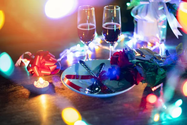 Valentines dinner romantic love concept / Romantic table setting decorated with fork spoon on plate and couple champagne glass roses with candle and colorful light on wooden table dinner at night