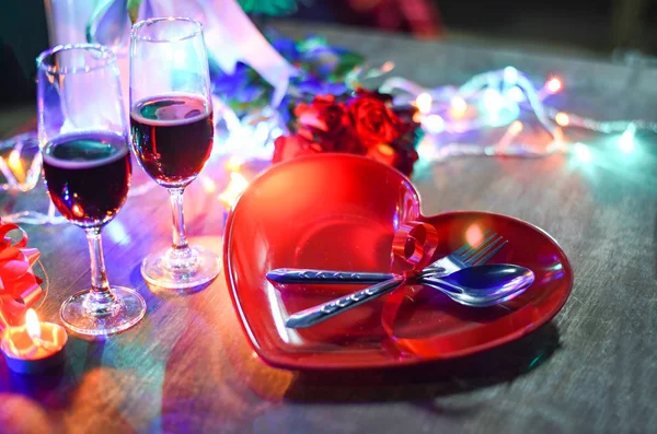 Valentines dinner romantic love concept / Romantic table setting decorated with fork spoon on heart plate champagne glass wine roses with candlelight on wooden table dinner night light background