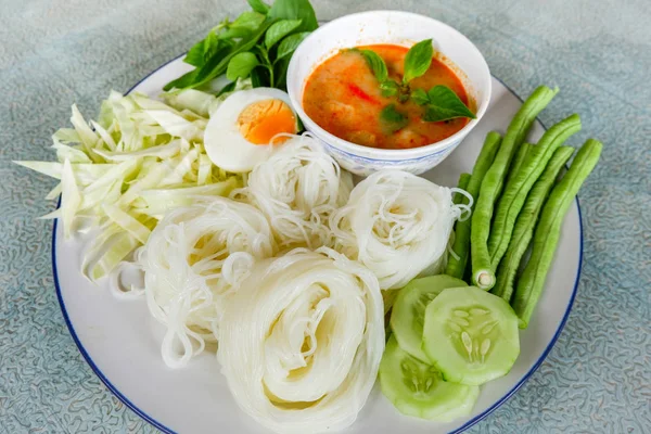 Thai rice noodle or rice vermicelli noodle and curry soup sauce on plate with vegetable yardlong , cucumber  bean and egg / Thai style food delicious