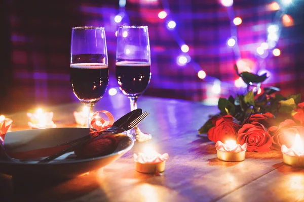 Valentines dinner romantic love concept / Romantic table setting decorated with Red heart fork spoon on plate and couple champagne glass wine roses with candlelight on wooden table dinner at night