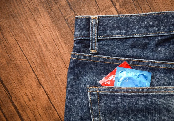 Condoms package in jeans / Colorful of Condom in back pocket blue jeans on wooden background - Prevent Pregnancy or sexually transmitted disease concept