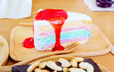 gökkuşağı krep pasta tabağı / lezzetli tatlı tatlı renkli krep pasta gökkuşağı üzerinde çilek soslu kek ahşap plaka üzerinde tepesinde 