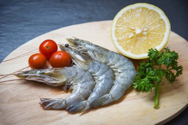 Kesme tahtası üzerinde / taze deniz ürünleri karides karides okyanus gurme çiğ karides domates limon ve yeşil maydanoz koyu arka plan üzerinde 