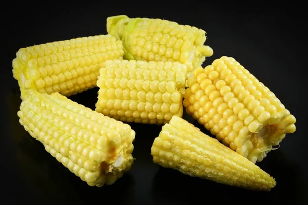 Close up of young baby sweet corn ear in fresh corn cob on black background
