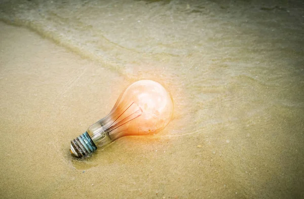 Ideenkonzept Glühbirne am Strand mit orangefarbener Beleuchtung auf Sand — Stockfoto