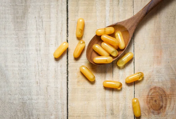 Royal jelly capsules in wooden spoon and wood table background — Stock Photo, Image