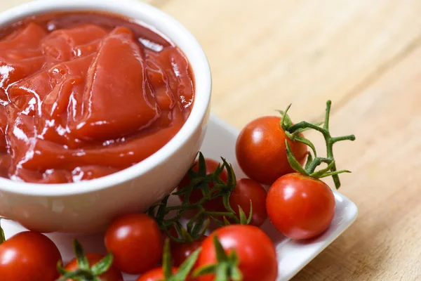 Ketchup in cup and fresh tomatoes on white plate — Stock Photo, Image