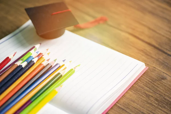 Pensil berwarna diatur dan topi kelulusan pada kertas putih notebook ba — Stok Foto