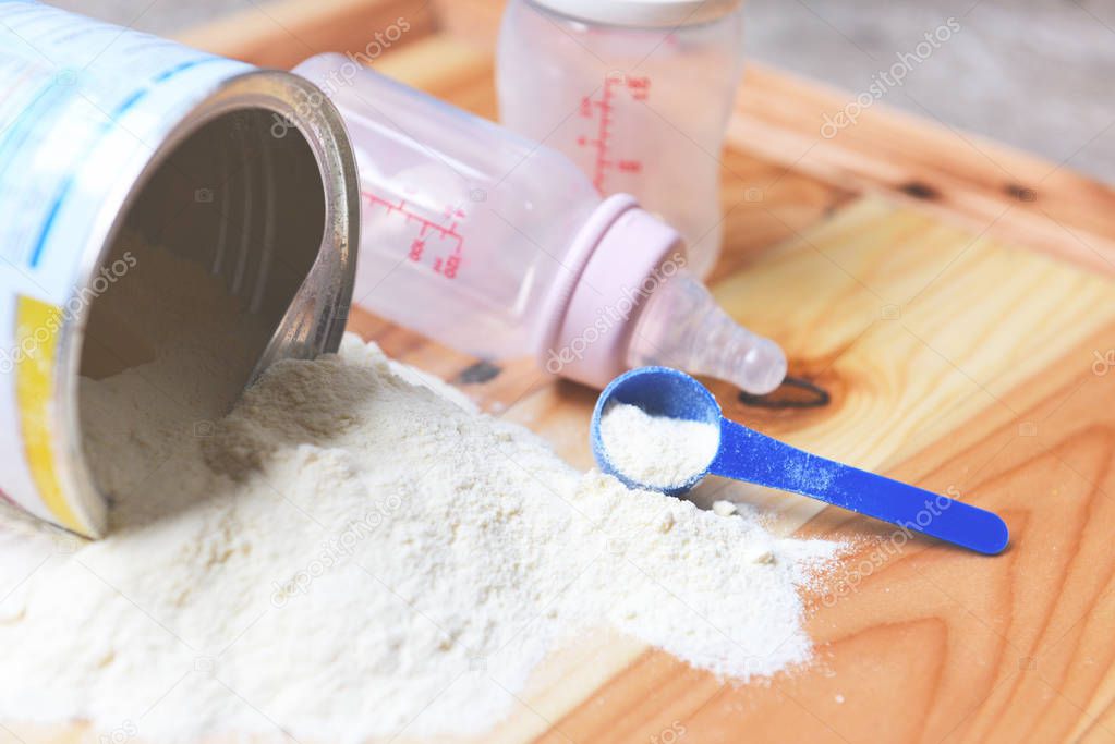 Milk powder can with spoon and baby bottle milk on wooden table