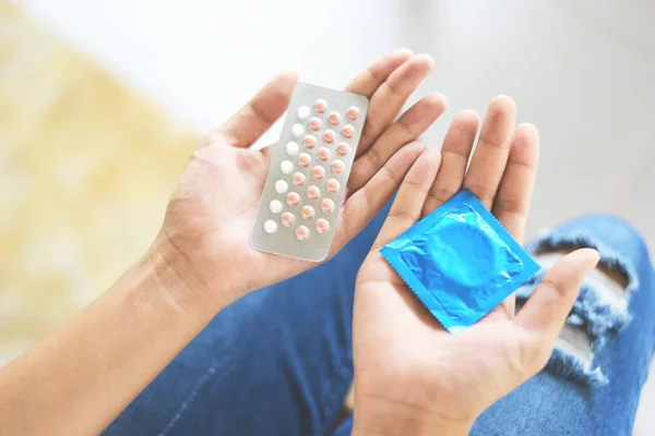 Mulher segurando pílulas de contracepção e preservativo na mão - Birth con — Fotografia de Stock