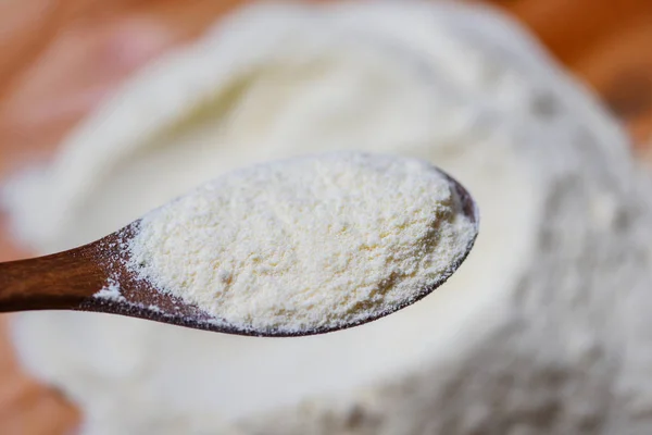 Milk powder on a wooden spoon with heap of powdered organic milk