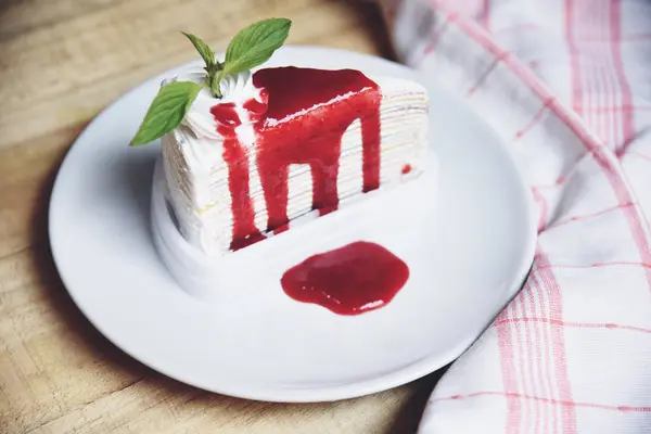 Crape cake slice with strawberry sauce on white plate on wooden