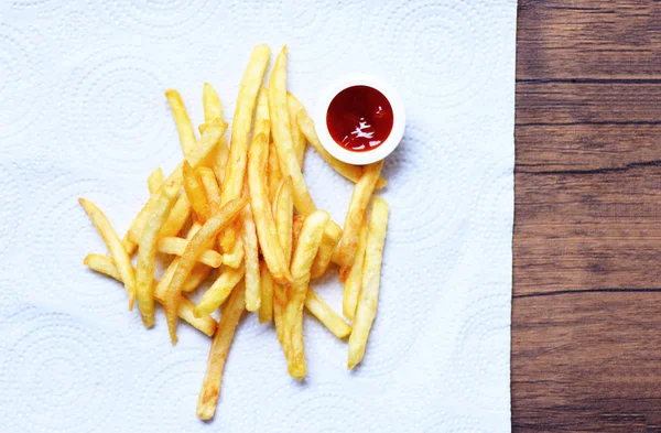 Batatas fritas em papel branco com ketchup em madeira — Fotografia de Stock