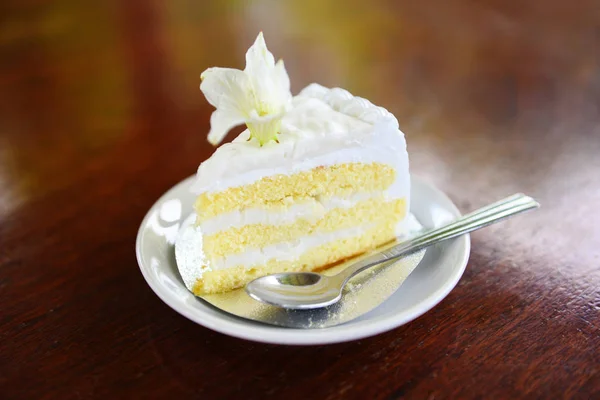 Ломтик торта на белом поддоне с цветком на фоне деревянного стола — стоковое фото