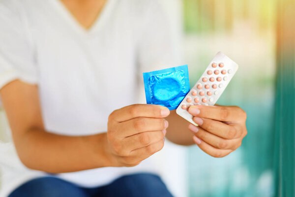 Young woman holding contraception pills and condom in hand - Bir