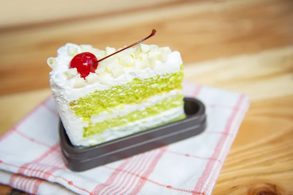 Green cake slice with cherry fruit and cream on white palte on t