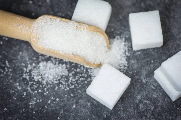 Azúcar blanco y terrones de azúcar en la cucharada de madera con fondo oscuro — Foto de Stock