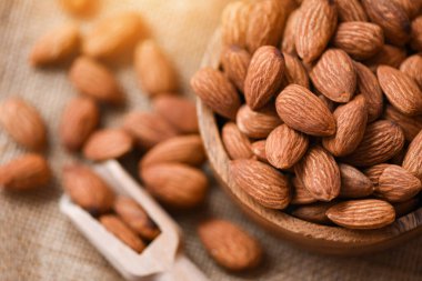 Masa arkasındaki ahşap kasede badem fıstığı ve kavrulmuş badem.