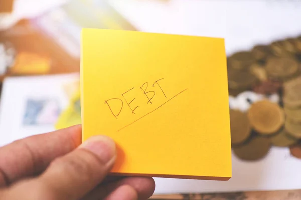 Debt concept with write debt on paper in hand and coins on table background
