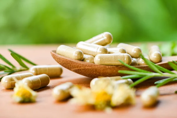 Herbal capsules from herbs healthy lifestyle / Herbal medicine extract from nature Non-toxic drug organic product on wooden spoon and wild flower rosemary on green background