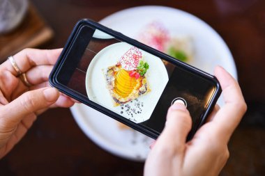Yemek fotoğrafçısı kadın elleri akıllı telefon / fotoğraf yiyeceği ile fotoğraf keki yapıyor ve sosyal ağlarda restoranda kameralı akıllı telefonla paylaşıyor. 