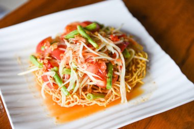 Papaya salatası baharatlı beyaz tabakta çıtır şehriye, fasulye ve baharatlı baharatlı baharatlı baharatlı fasulye ve sarımsaklı domates.