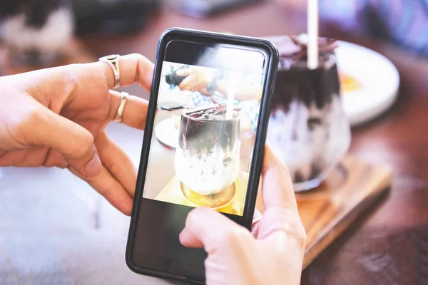 Food photography woman hands make photo cocoa drink and cake with smartphone / taking photo food for post and share on social networks with camera smart phone in restaurant