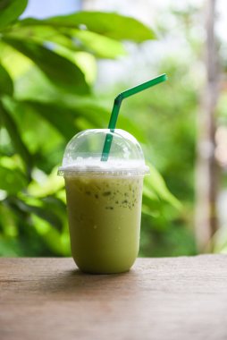 Buzlu içecekler yeşil çay smoothie / Matcha yeşil çay üzerinde süt ile ahşap masa üzerinde plastik cam ve doğa yeşil arka plan 