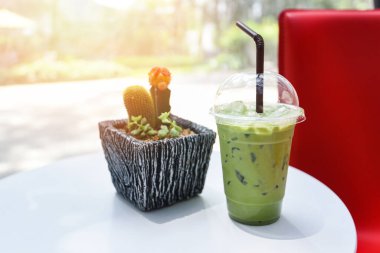 Buzlu içecekler yeşil çay smoothie / Matcha yeşil çay üzerinde süt ile ahşap masa üzerinde plastik cam ve doğa yeşil arka plan