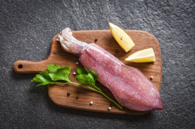 Ahşap kesme tahtasındaki çiğ mürekkep balığı ve limonlu maydanoz deniz ürünleri pazarı / taze mürekkep balığı ahtapot veya pişmiş salata restoranı için mürekkep balığı.  
